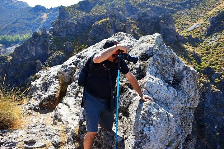 Ein Fotograf, der von einem Felsvorsprung in den Bergen ein Foto macht