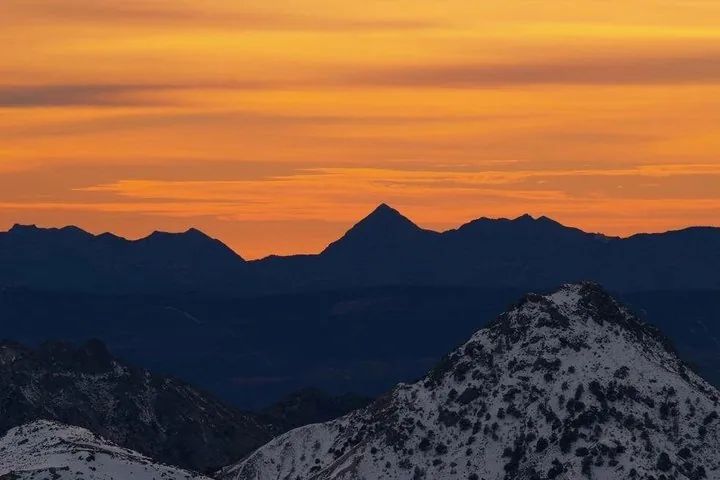 Silhouette d'un sommet de montagne se détachant sur un ciel orange de coucher de soleil